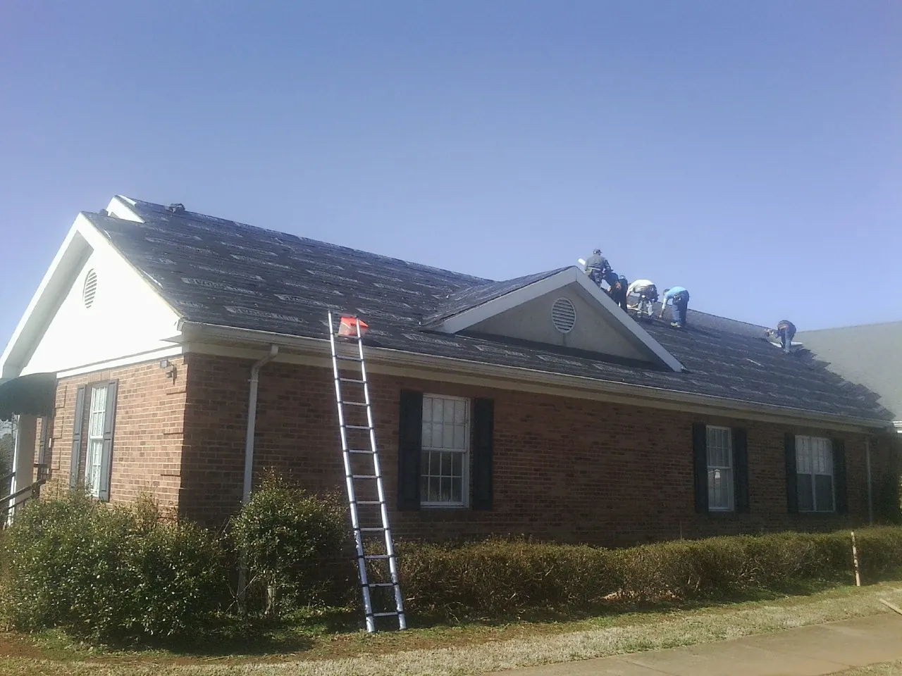 Crew tearing shingles off a brick ranch roof with a ladder set — Emergency Roof Repair work by our crew in Cadiz