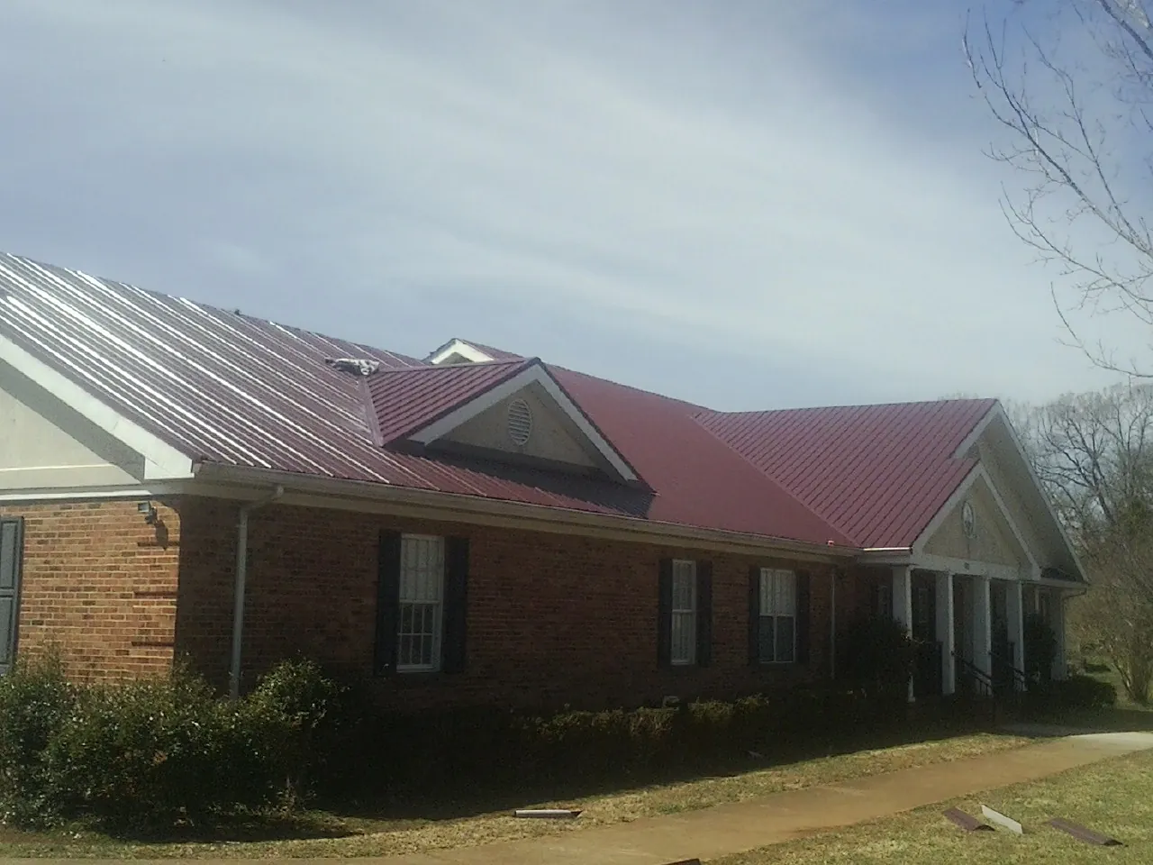 Red metal roof with gabled entries on a long brick building, from a Hail Damage Roof Repair job in Cadiz