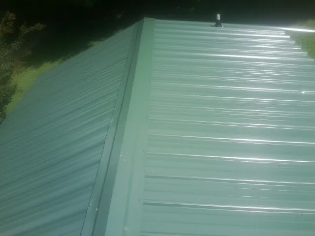 New green metal panels meeting at the ridge of a roof — Flat Roof Repair work by our crew in Cadiz
