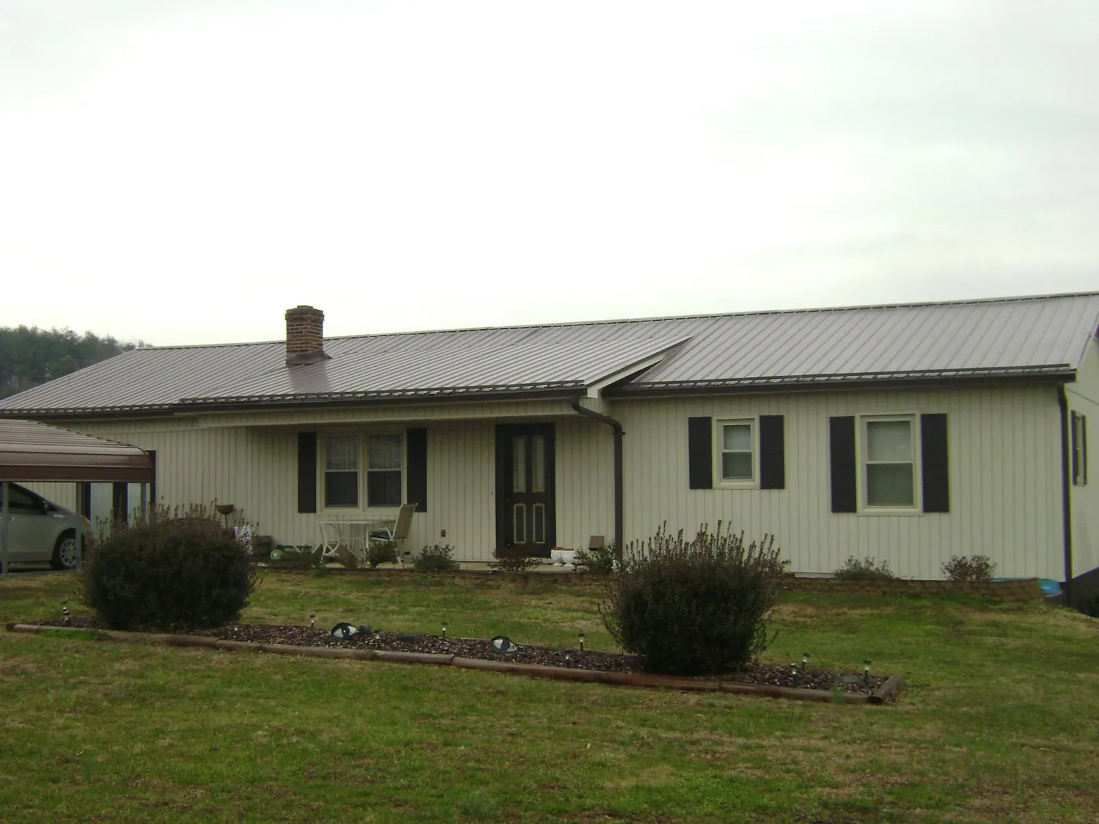 Brown metal roof on a cream sided ranch home with a brick chimney in Cadiz