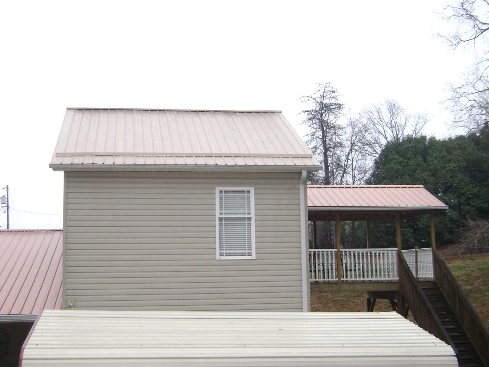 Tan metal roofs on a two story addition and attached porch, from a Roof Replacement job in Cadiz